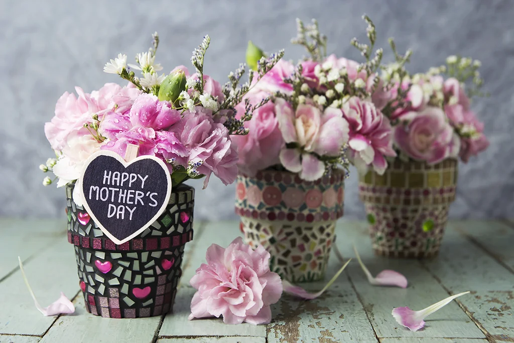 Three vases, each with a unique pattern, are arranged on a wooden surface. The left vase has a heart-shaped design with the message "Happy Valentine's Day" and pink roses. The middle vase has a black and white pattern with pink roses and a heart-shaped design with the message "Happy Valentine's Day" and white roses. The right vase has a black and white pattern with pink roses and a heart-shaped design with the message "Happy Valentine's Day" and white roses. The vases are set against a grayish-blue wall, creating a warm and inviting atmosphere.
